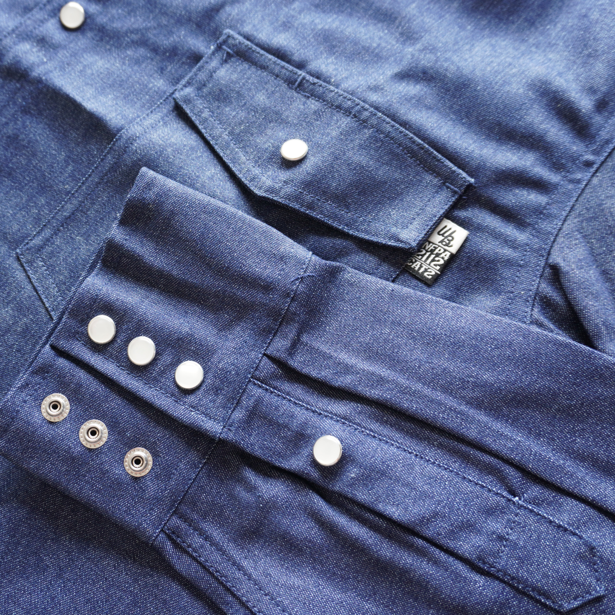 Close-up of a blue denim shirt with buttons and a brand tag.