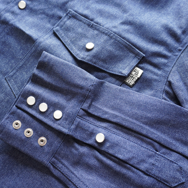Close-up of a blue denim shirt with buttons and a brand tag.