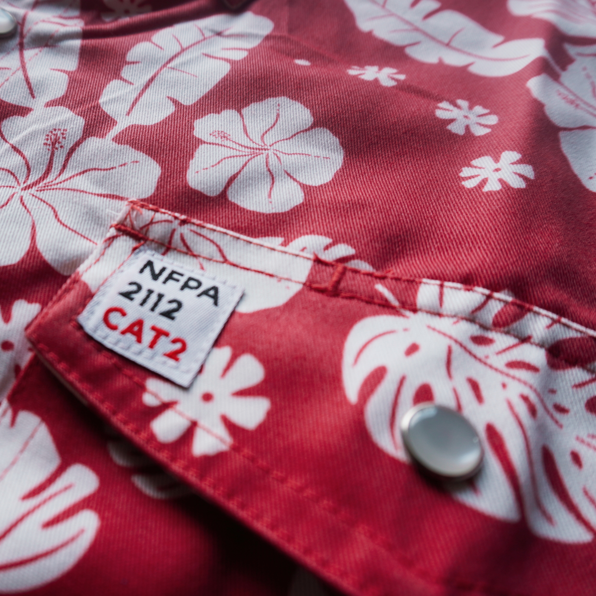 Red fabric with white floral patterns and NFPA 2112 CAT2 label.