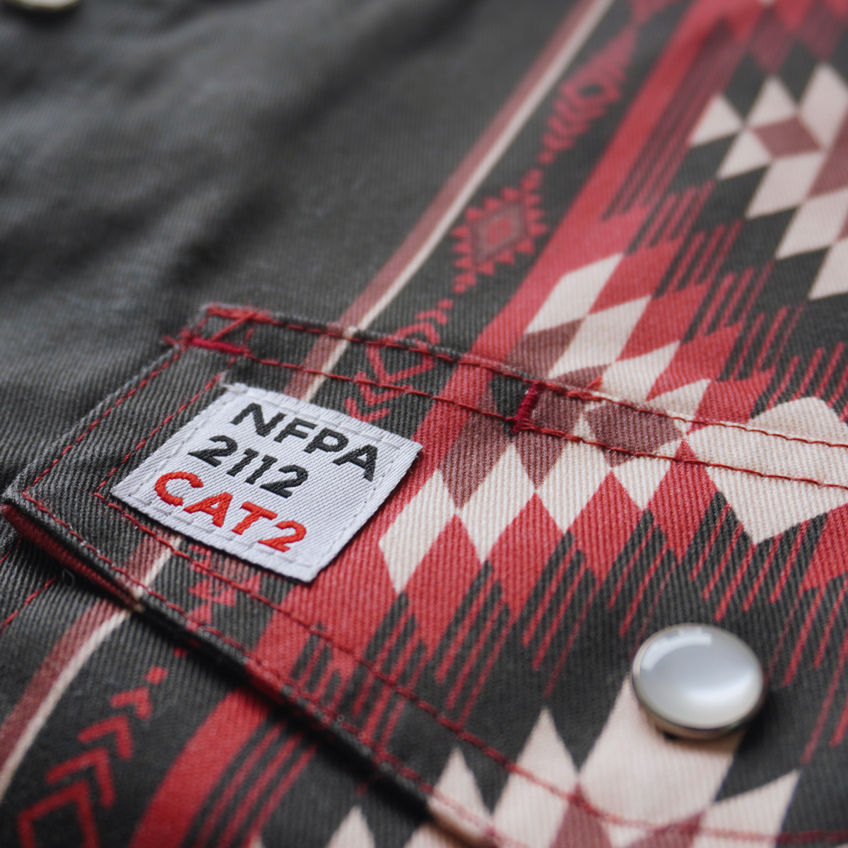Close-up of a label on a garment with NFPA 2112 CAT2 text on a patterned fabric background.