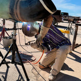 Person welding a large metal object outdoors with a truck in the background.