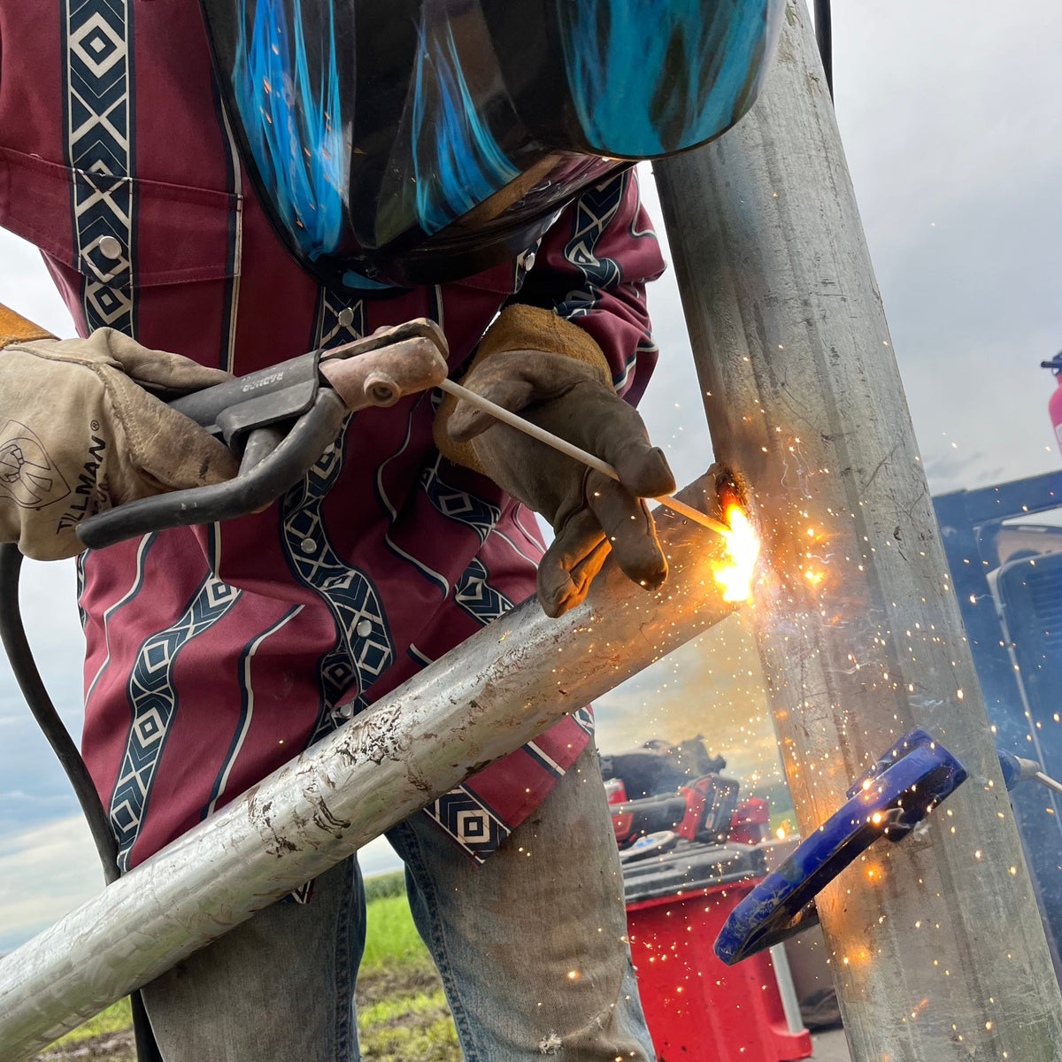 Person welding a metal pole with sparks flying, wearing protective gear.