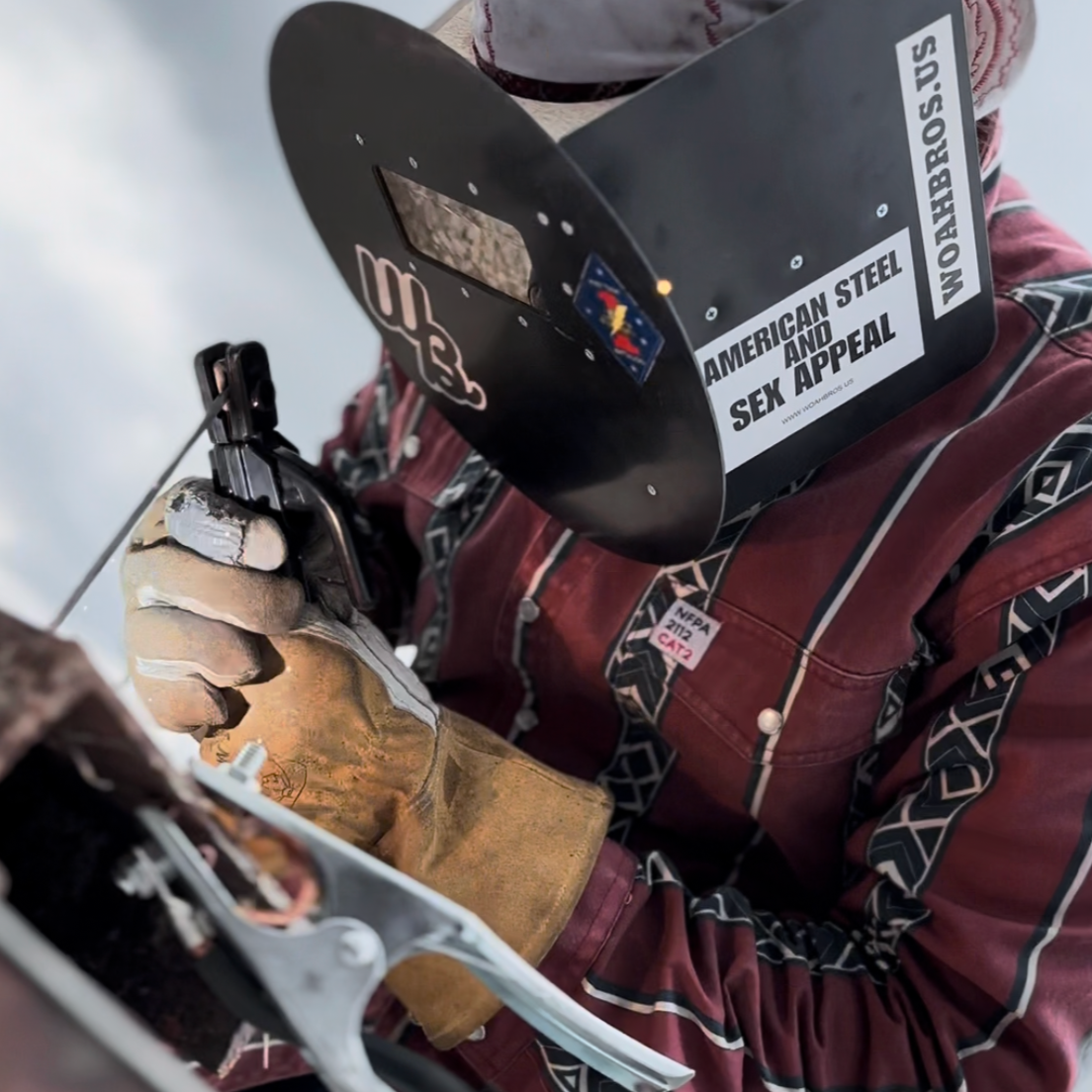 Person wearing a welding helmet with visible branding, holding a welding tool.