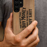 Close-up of a man’s hand holding a Samsung phone with the Big Boy Money tough case, showing the woodgrain design and bold black lettering, “You want that Big Boy Money, you have to do that Big Boy Shit.”